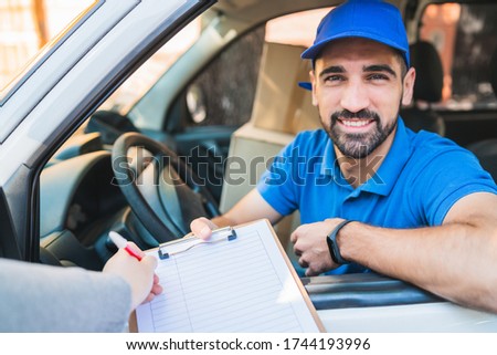 Portrait of a delivery man in van while customer putting signature in clipboard. Delivery and shipping concept.