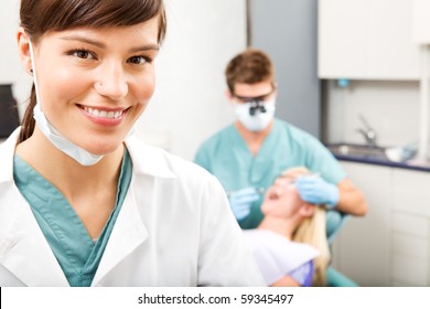 A portrait of a dental assistant smiling at the camera with the dentist working in the background - Powered by Shutterstock