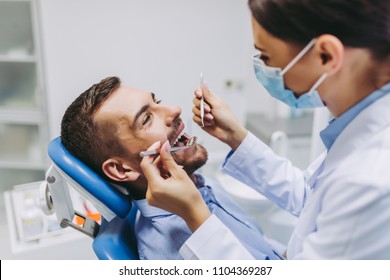 Portrait Of Dentist In Medical Mask Checking Patient Teeth With Mirror In Dental Clinic