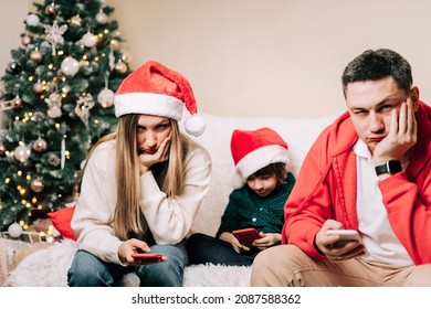 Portrait Of Depressed Family With Son Playing Cell Phone During New Year Party. Tired Mom And Dad Having A Stressful Time While Kid Using With Mobile Phone. Family Dispute After Christmas Celebration.