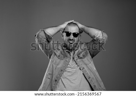 Portrait of depressed man in casual clothes and sunglasses expressing despair while keeping his hands on his head