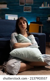 Portrait Of Depressed Woman With Mental Health Problems Sitting On Floor And Hugging Pillow In Living Room. Anxious Sad Person Dealing With Chronic Disease Difficulties And Depression At Home.