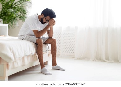 Portrait Of Depressed Young Indian Man Sitting On Bed At Home, Upset Millennial Eastern Guy Burying Head In Hands, Suffering Life Problems Or Mental Breakdown, Feeling Despair, Copy Space - Powered by Shutterstock