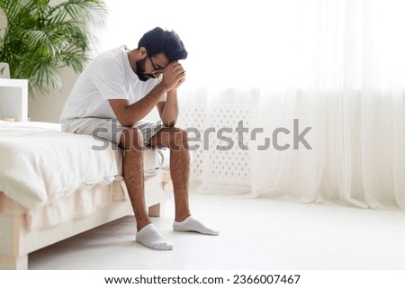 Portrait Of Depressed Young Indian Man Sitting On Bed At Home, Upset Millennial Eastern Guy Burying Head In Hands, Suffering Life Problems Or Mental Breakdown, Feeling Despair, Copy Space