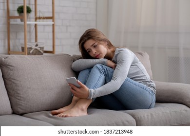 Retrato de una joven deprimida sentada en el sofá con un smartphone en las manos. Milenesa sufriendo de ciberacoso o de una mala ruptura. Concepto de salud mental