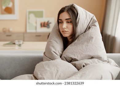 Portrait of depressed young woman wrapped in blankets at home struggling with mental health issues, copy space - Powered by Shutterstock