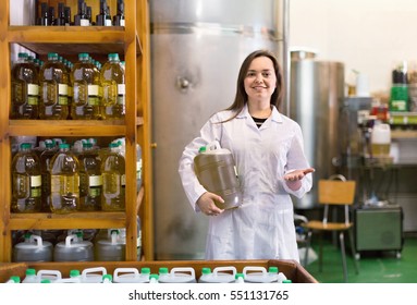 Portrait of diligent positive female posing with olive oil containers inside factory - Powered by Shutterstock