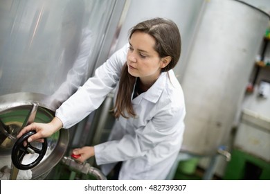 Portrait of diligent smiling female engineer rotating valve on tank inside factory - Powered by Shutterstock