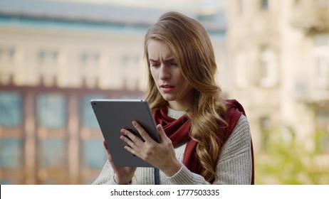 Portrait Of Disappointed Girl Surfing Internet By Tablet Computer Outdoors. Closeup Upset Woman Looking Tablet Screen In Urban Background. Serious Hipster Girl Reading News On Tablet At City Street.