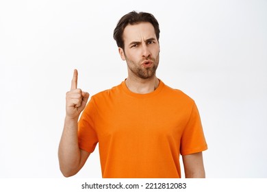 Portrait Of Disappointed Guy Pointing Finger Up, Grimacing, Being Upset, Standing In Orange Tshirt