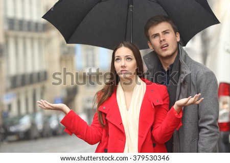 Portrait of a disgusted couple annoyed in a rainy day under the rain and an umbrella in winter