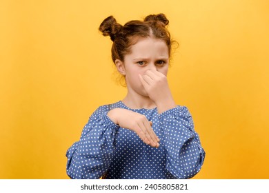 Portrait of disgusted preteen girl child smelling stinky smell and frowning, angry looking at camera, standing posing on yellow color background wall in studio with copy space. People emotion concept