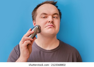 Portrait Of Disheveled Adult Man Shaving Stubble With Electric Razor, Blue Studio Background