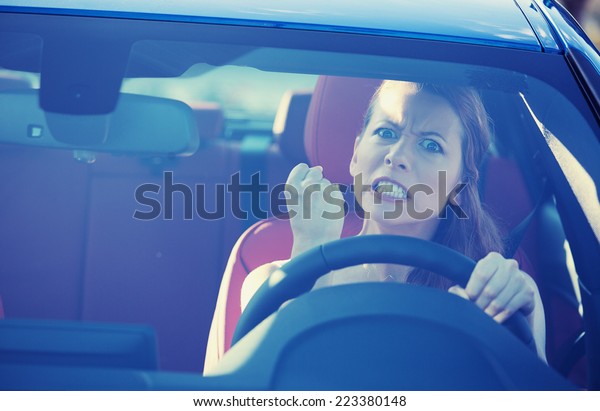 Portrait displeased angry pissed off\
aggressive woman driving car, shouting at someone in traffic hand\
fist up in air front windshield view. Emotional intelligence\
concept. Negative human\
expression