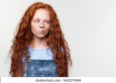 Portrait of displeased cute freckles little girl with ginger hair, looks with disgust at the copy space on the left side, tands over white background. - Powered by Shutterstock