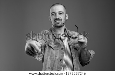 Portrait of displeased man in denim jacket expressing disrespect while pointing at you and holding his spectacles in hand