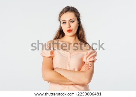 Portrait of displeased offended girl with dark hair, keeps arms folded, looks angrily to the camera, doesn't agree with somebody's opinion. Studio shot, white background
