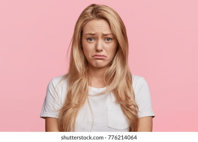 Portrait of displeased upset female frowns face as going to cry, being discontent and unhappy as can`t achieve goals, isolated over pink studio background. Dissapointed young woman has troubles