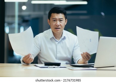 Portrait Of Dissatisfied Business Investor, Asian Businessman Working In Office, Looking At Camera And Holding Documents, Disappointed With Report