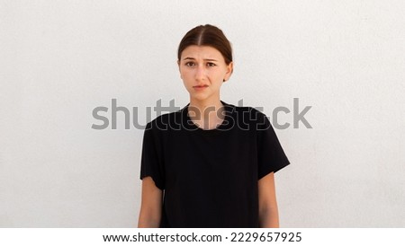 Portrait of distrustful young woman looking at camera over white background. Caucasian woman wearing black T-shirt posing with doubtful expression. Disbelief and doubt concept