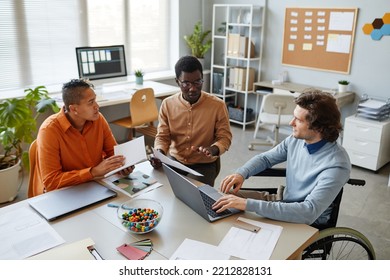 Portrait of diverse business team discussing project at meeting table focus on young man using wheelchair in foreground, inclusivity at workplace - Powered by Shutterstock