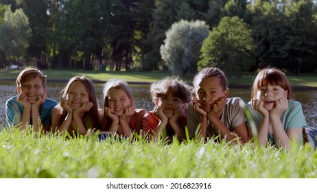 Portrait of diverse children lying on grass in park and smiling at camera. Happy multiethnic teen friends having fun outdoors looking at camera - Powered by Shutterstock