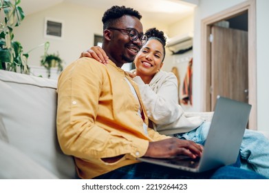 Portrait Of A Diverse Couple Enjoying Time At Home And Using Laptop While Sitting On Sofa. Focus On An African American Man Holding Computer On His Lap And Spending Time With His Hispanic Wife.