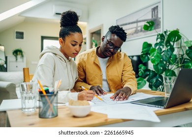 Portrait of a diverse couple sitting at the table at home and using a laptop and a house plan while making a financial strategy for building a new home. Looking in the blueprints. Moving in together. - Powered by Shutterstock