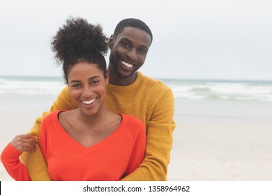 Portrait of diverse couple standing at beach on a sunny day. They are smiling and looking at camera - Shutterstock ID 1358964962