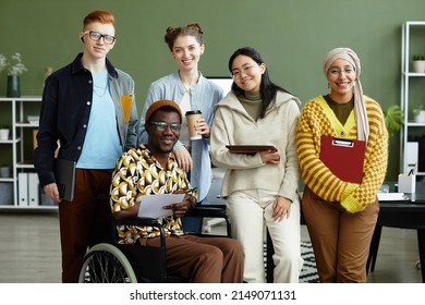 Portrait of diverse creative team looking at camera with cheerful smiles while posing in office, wheelchair user inclusion