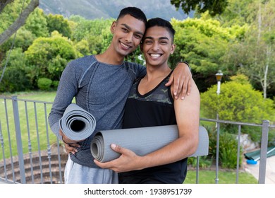 Portrait of diverse gay male couple holding yoga mats and smiling on balcony. staying at home in isolation during quarantine lockdown. - Powered by Shutterstock