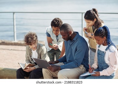 Portrait Of Diverse Group Of Kids With Male Teacher Using Laptop Outdoors During Summer School Lesson, Copy Space