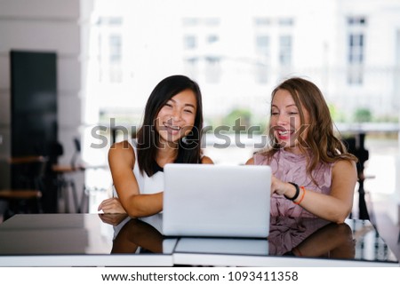 Portrait of a diverse team of two coworkers (a Chinese Asian woman and a Caucasian white woman) looking over a DCF cashflow model on a laptop computer in the day. 