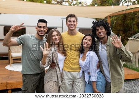 Portrait of diverse young friends posing and smiling at camera near trailer, enjoying autumn weekend on camping trip. Happy millennial people traveling together in motorhome, having fun
