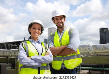 Portrait diversity male and female engineer work together on roof top of site line . Portrait of engineer with green safety vest and white hard hat at building site looking at camera 