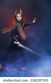 Portrait Of Divine Female Warrior Valkyrie Standing With A Sword In Her Hand. Epic Fantasy. Scandinavian Mythology. Dark Background With Smoke And Red Light.