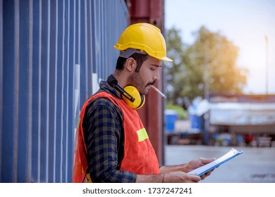 Portrait dock worker under working and checking production process on dock container warehouse by document ,wearing safety uniform ,ear phone and smoking cigarette.