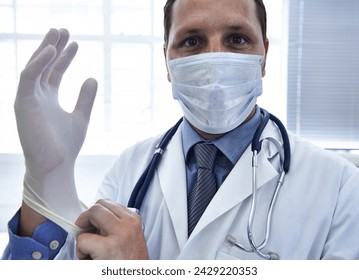Portrait, doctor and man put on gloves in mask for protection or safety in hospital. Face, medical professional and ppe to prepare for surgery, treatment or prevention of disease in healthcare clinic - Powered by Shutterstock