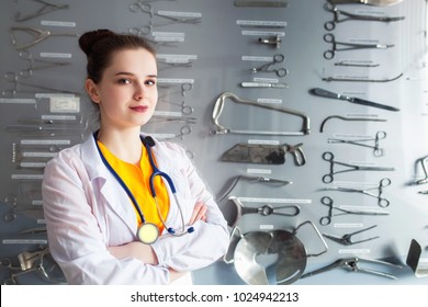 Portrait Of A Doctor On A Stand Background With A Surgical Instrument. Concept Young Student Girl Studying A Medical Tool