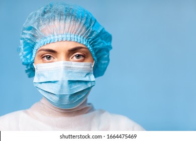 Portrait of a doctor, a young woman in a protective medical mask on her face and a cap on her head. looking seriously into the frame. on a blue background. surgeon. ambulance paramedic. copy space