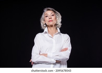 Portrait of a domineering, arrogant mature woman looking down and standing with her arms crossed isolated on a black background