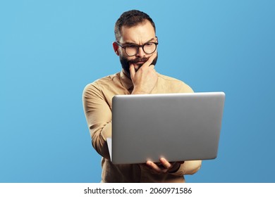 Portrait of a doubtful bearded man holding laptop computer isolated over blue background  - Shutterstock ID 2060971586