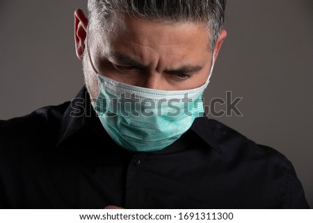 Portrait of downcast man with medical protection mask on gray studio background. Coronavirus quarantine concept.