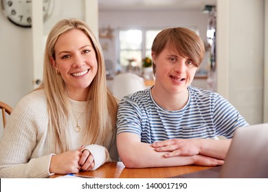 Portrait Of Downs Syndrome Man Sitting With Home Tutor Using Laptop For Lesson At Home