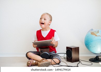 A portrait of down-syndrome school boy with tablet sitting on the floor.
