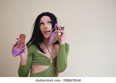 Portrait Of A Drag Queen Person Posing Holding Heels On Beige Background.