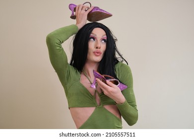 Portrait Of A Drag Queen Person Posing Holding Heels On Beige Background.