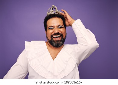 Portrait Of A Drag Queen Smiling On Purple Background. Bearded Man Wearing Makeup And Crown On Head.