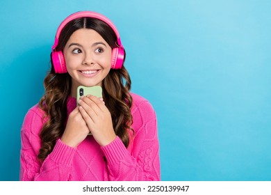 Portrait of dream brown curly hair teenage girl wear pink new wireless bluetooth headphones look itunes empty space isolated on blue color background