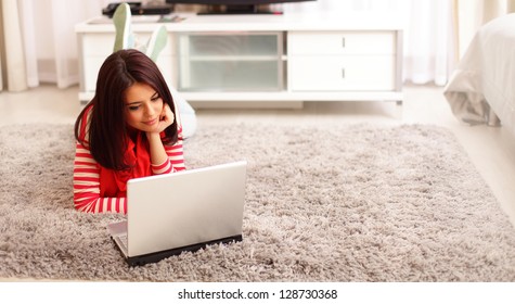 Portrait of dreamy smiling young woman using laptop while lying on floor at home - Powered by Shutterstock